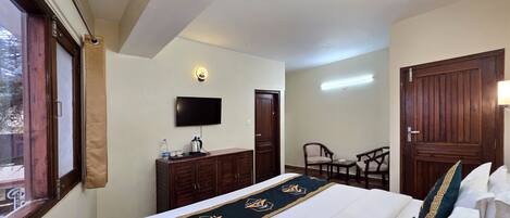 A hotel room with a bed, a television, a desk with a chair, and a wardrobe.