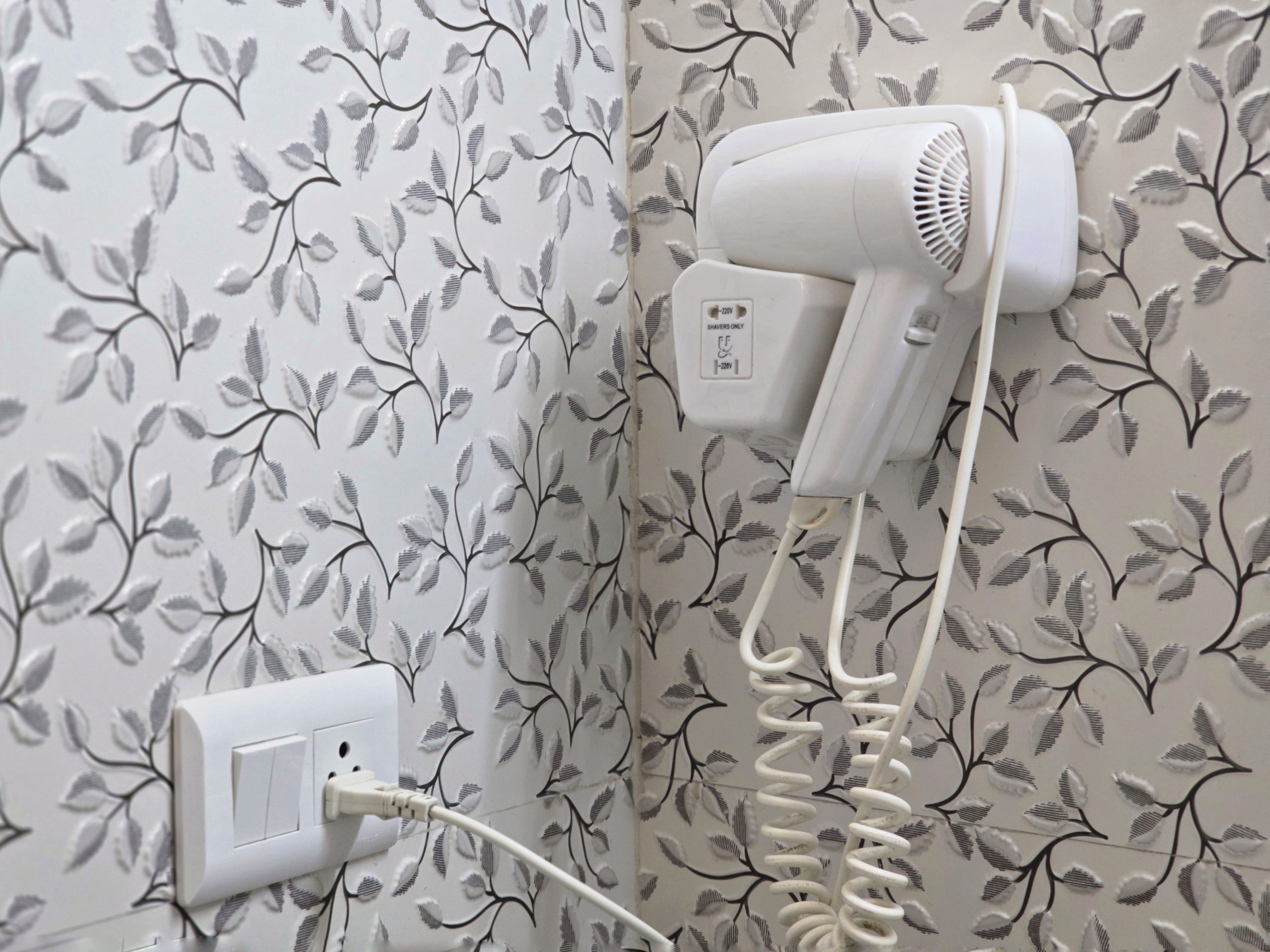 A hairdryer mounted on a wall with a floral wallpaper pattern.