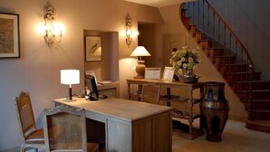 A dining area with a table, chairs, wall sconces, a lamp, a vase with flowers, and a staircase. - Domaine Rollan de by (Bégadan)