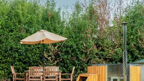 Eine Terrasse mit Holzmöbeln und einem Heizstrahler, umgeben von üppigem Grün.