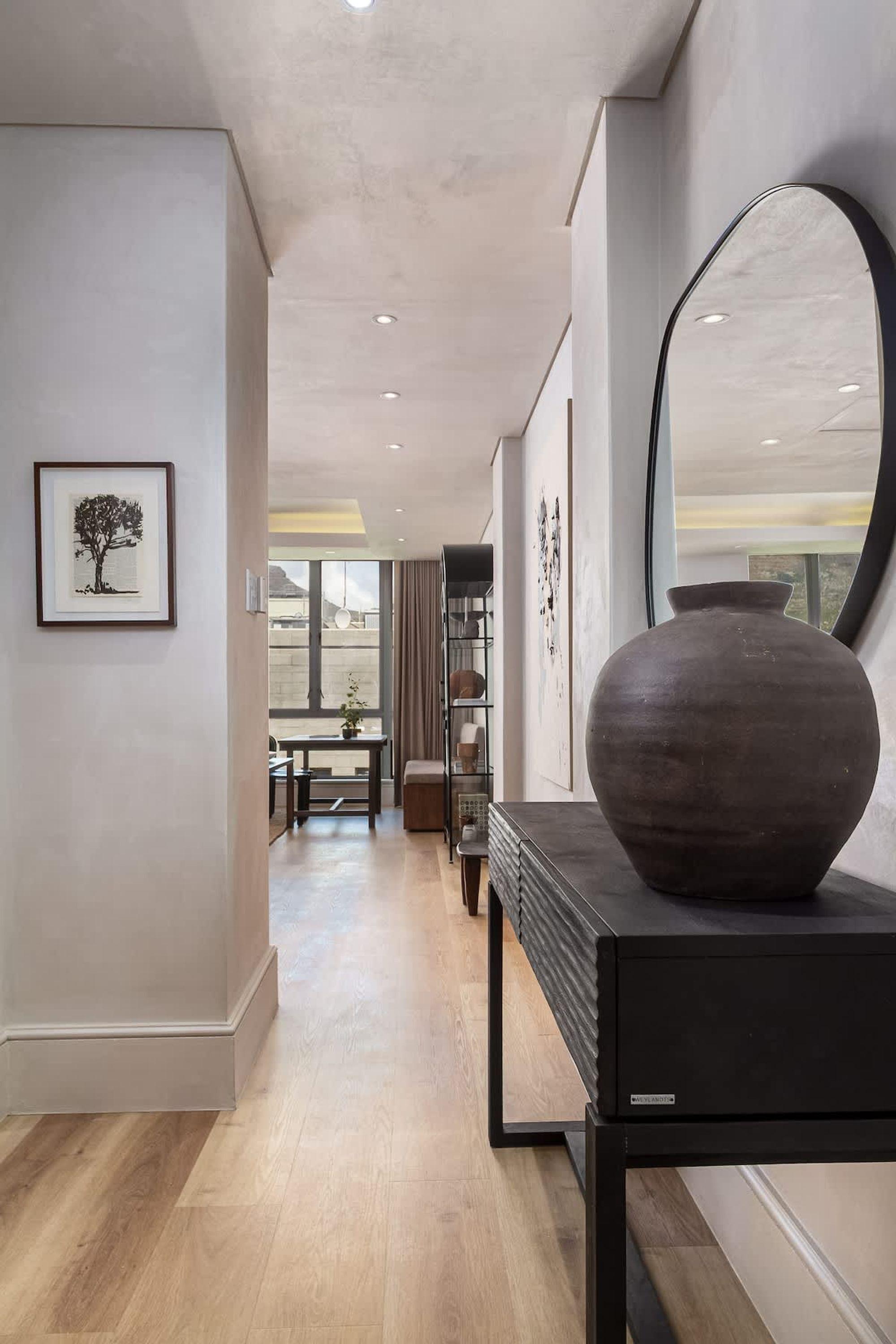 Un intérieur moderne avec un grand miroir, une console sombre et une œuvre d’art encadrée accrochée au mur.