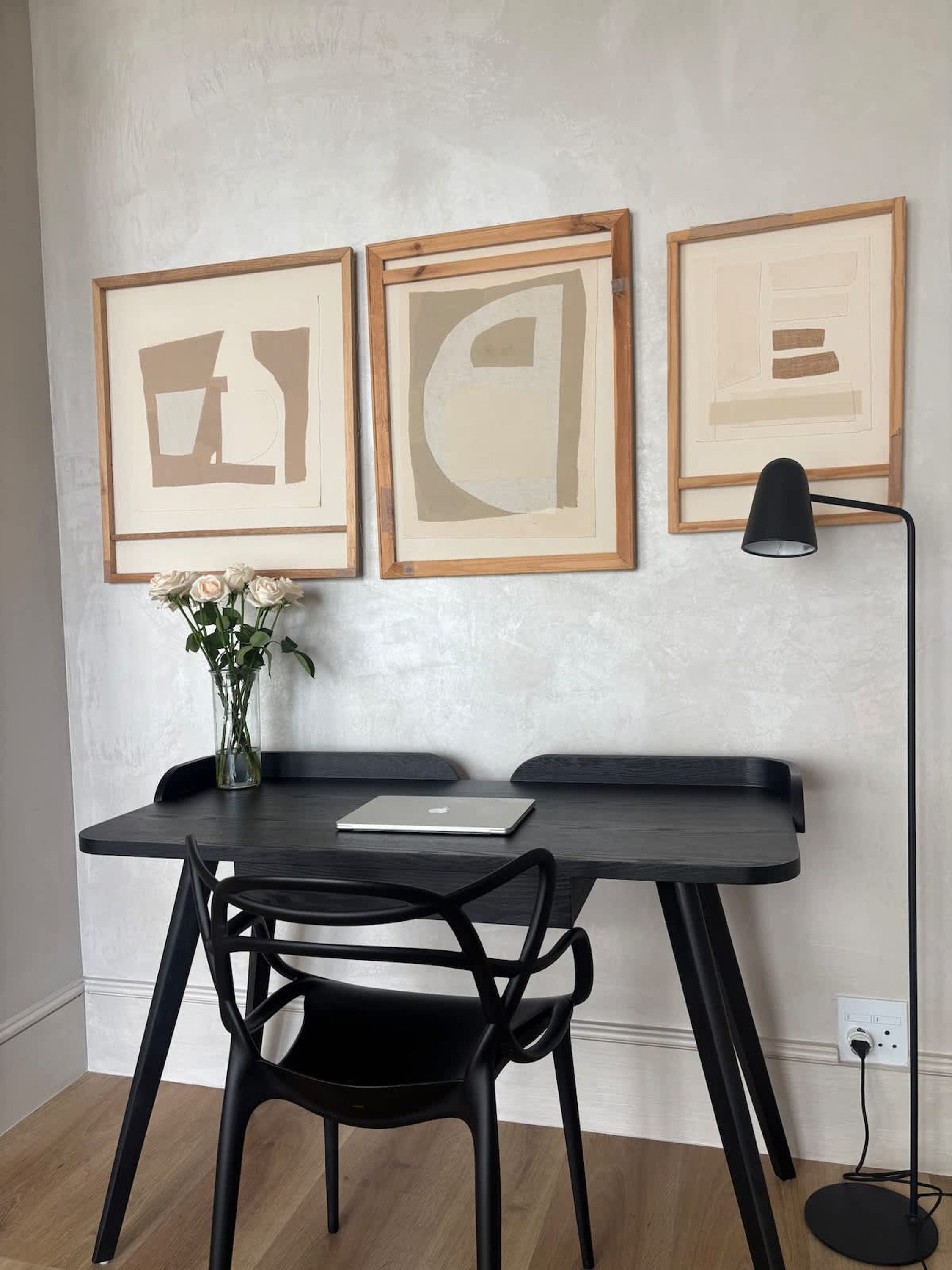 Un'area di lavoro moderna con una scrivania scura, una sedia nera e un portatile. Tre opere d'arte astratte incorniciate sono appese alla parete sopra la scrivania.