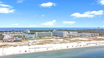 A coastal hotel with multiple buildings, a beach, and a clear sky.