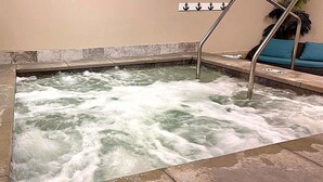 Een jacuzzi met een metalen reling, een bedieningspaneel aan de muur en een blauwe, beklede bank.