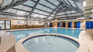 Een binnenzwembad met een jacuzzi, overdekt dak en zitgedeeltes.