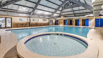 An indoor swimming pool with a hot tub, a covered roof, and seating areas.