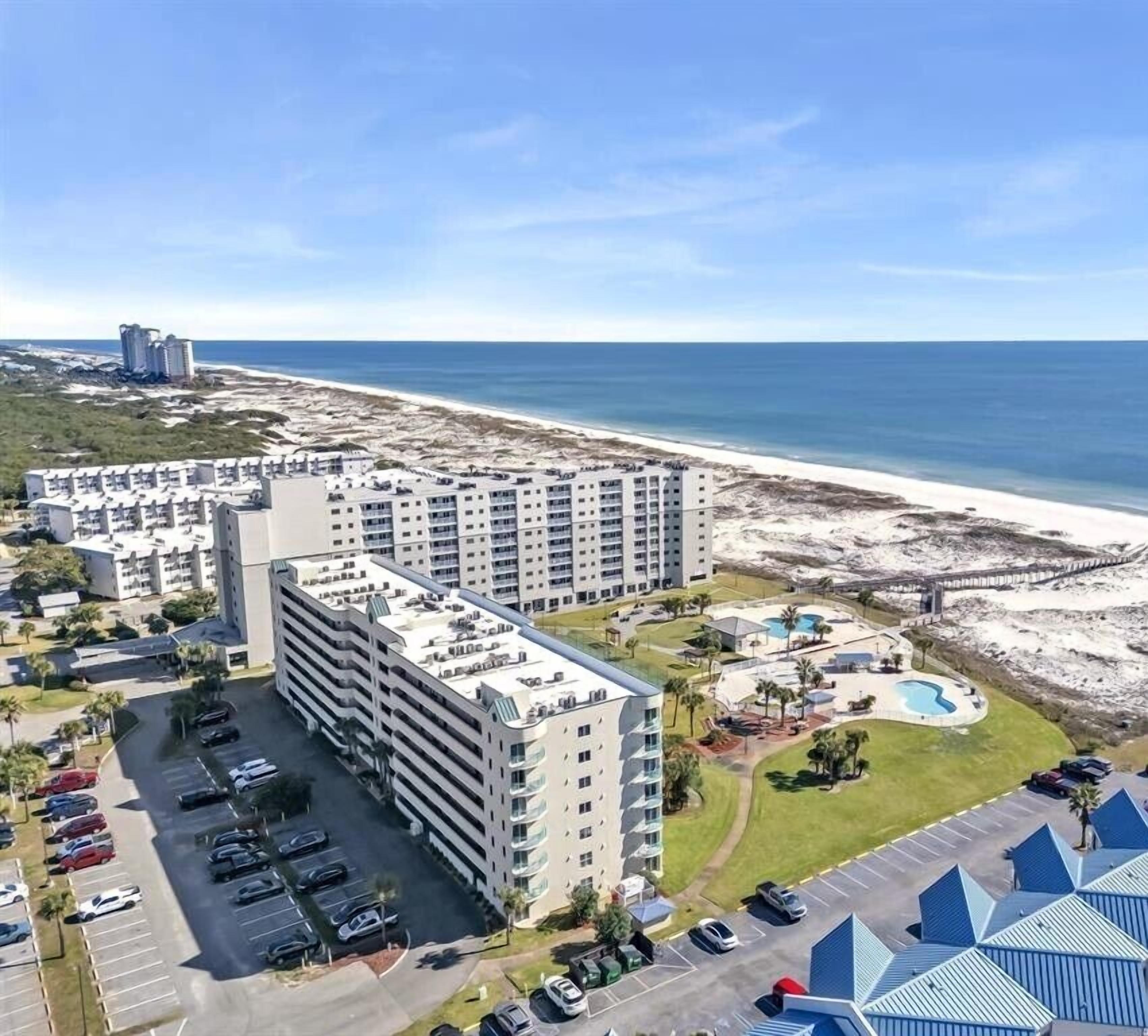 A high-rise hotel with multiple floors, a parking lot, and a beach view.