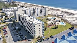 Een hoog hotel met meerdere verdiepingen, een parkeerplaats en uitzicht op het strand.