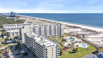 A high-rise hotel with multiple floors, a parking lot, and a beach view.