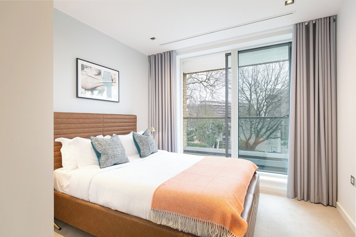 Ein Schlafzimmer mit Bett, Fenster und Blick auf Bäume.