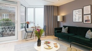 Un soggiorno moderno con un divano verde, un tavolo da pranzo con sedie, un vaso con fiori e un'ampia finestra con tende.