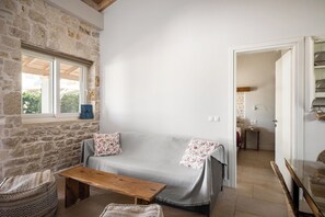Ein gemütliches Zimmer mit Steinwand, einer Couch, einem Holztisch und einem Korbstuhl.