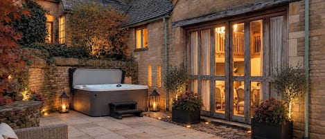 A stone building with a hot tub, outdoor seating, and a large window overlooking a dining area.