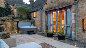 A stone building with a hot tub, outdoor seating, and potted plants. - Willowberry Barn - Exclusive Home with Hot Tub (Weston Subedge)