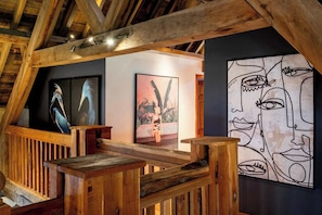 Un escalier en bois avec une rampe, un mur orné de tableaux encadrés et un plafond avec des poutres apparentes.