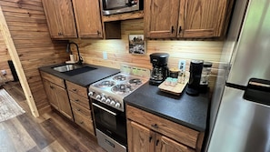 Una cocina compacta con gabinetes de madera, estufa, fregadero y cafetera.