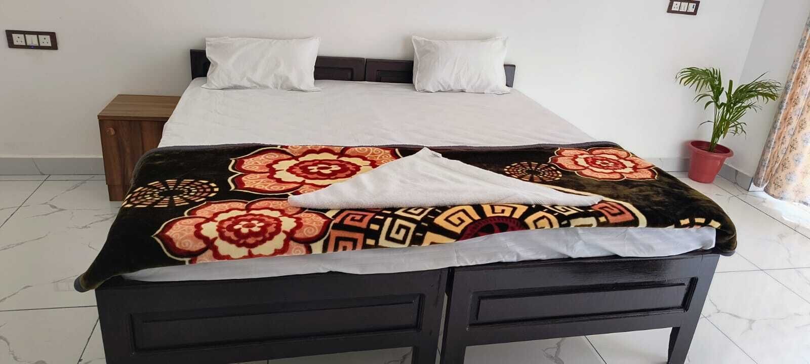 Een bed met een geborreld sprei, een nachtkastje, een bloempot en een gordijn.