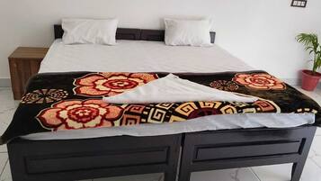 Een bed met een geborreld sprei, een nachtkastje, een bloempot en een gordijn.