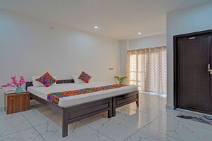 Quarto de hotel com cama, mesa de cabeceira, planta em vaso e uma porta.
