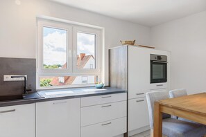 Eine moderne Küche mit Fenster, weißen Schränken, einem Holztisch und einem eingebauten Backofen.