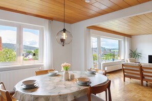 A dining area with a round table, chairs, a vase with flowers, and a hanging light fixture. - Lotterberg Holiday Apartment (Gudensberg)
