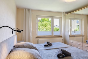 A bedroom with a bed, a window with curtains, a radiator, and a mirror. - Lotterberg Holiday Apartment (Gudensberg)