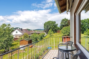 A balcony with a table and chairs, a view of a green landscape, and a wooden structure in the background. - Lotterberg Holiday Apartment (Gudensberg)