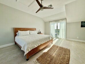 A bedroom with a bed, a ceiling fan, a nightstand, a rug, and a view through a glass door. - Sanibel Retreat - Walk to the Beach! (sanibel)