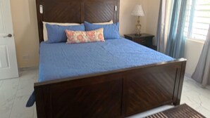 A bedroom with a wooden bed, a nightstand, a lamp, and a window with curtains. - Serene Family - 4Bed/4Bath Private Ensuite (Cruz Bay)