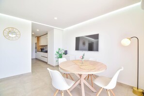 A modern kitchen with white cabinets, a dining area with a round table and white chairs, and a flat-screen TV on the wall. - Cozy 1-bedroom apartment in beautiful Portimão with AC (Portimão)