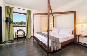 Ein Bett mit Baldachin, ein Holzgestell, ein Stuhl, ein Schreibtisch und Blick durch ein Fenster mit Vorhängen.