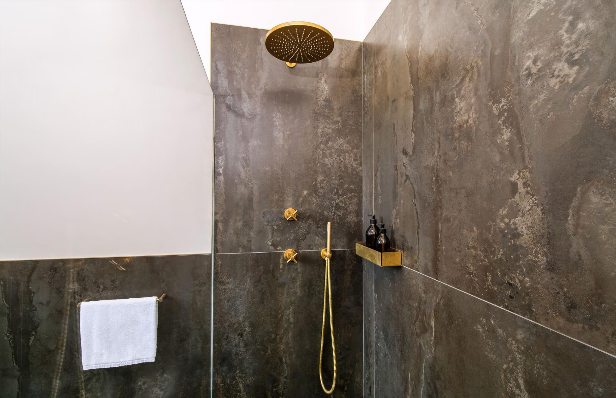 A shower with a handheld showerhead, a towel rack, and a soap dispenser.