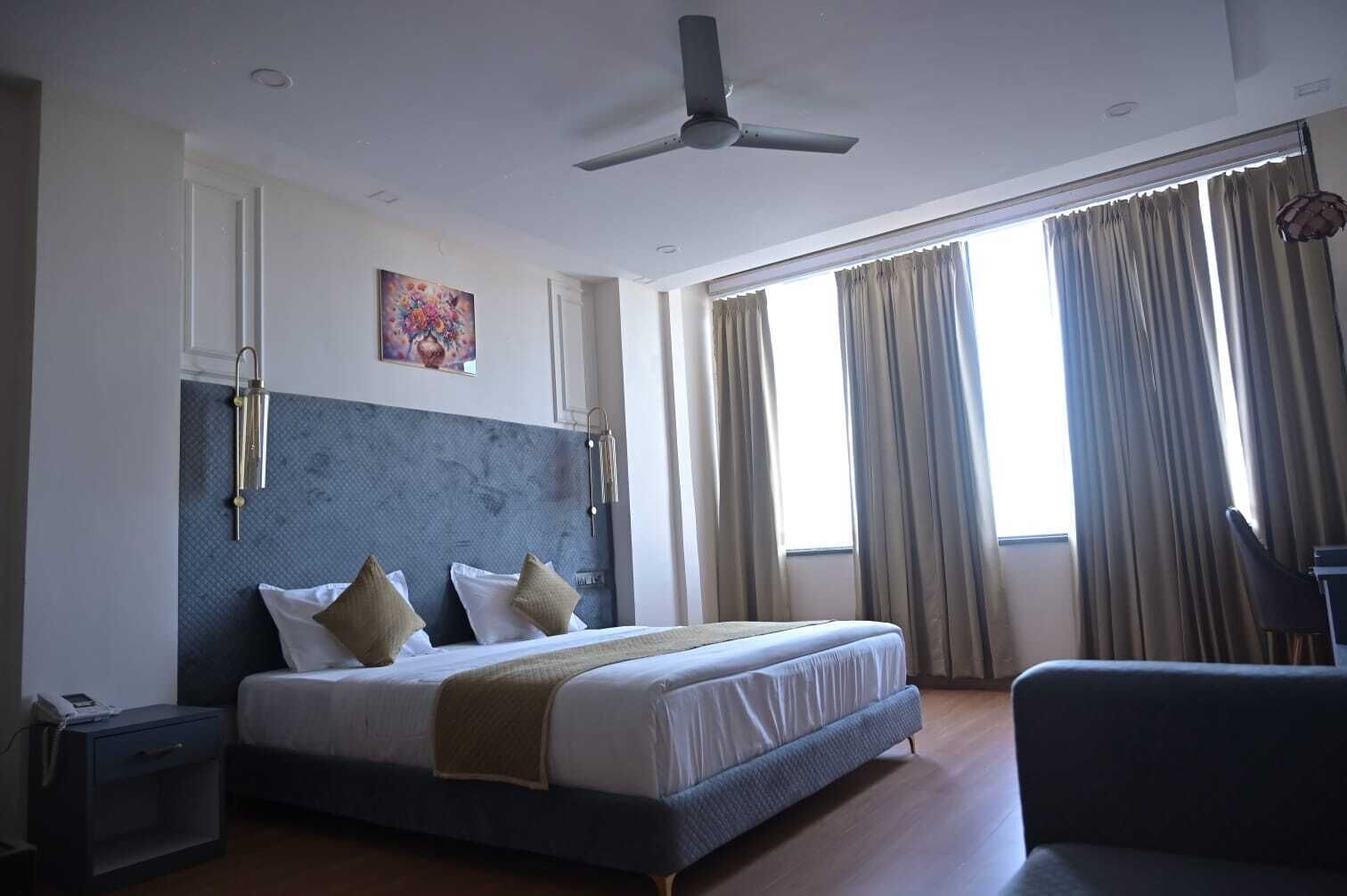 Une chambre d’hôtel équipée d’un lit, d’un bureau, d’une chaise, d’un ventilateur de plafond et d’une fenêtre avec des rideaux.