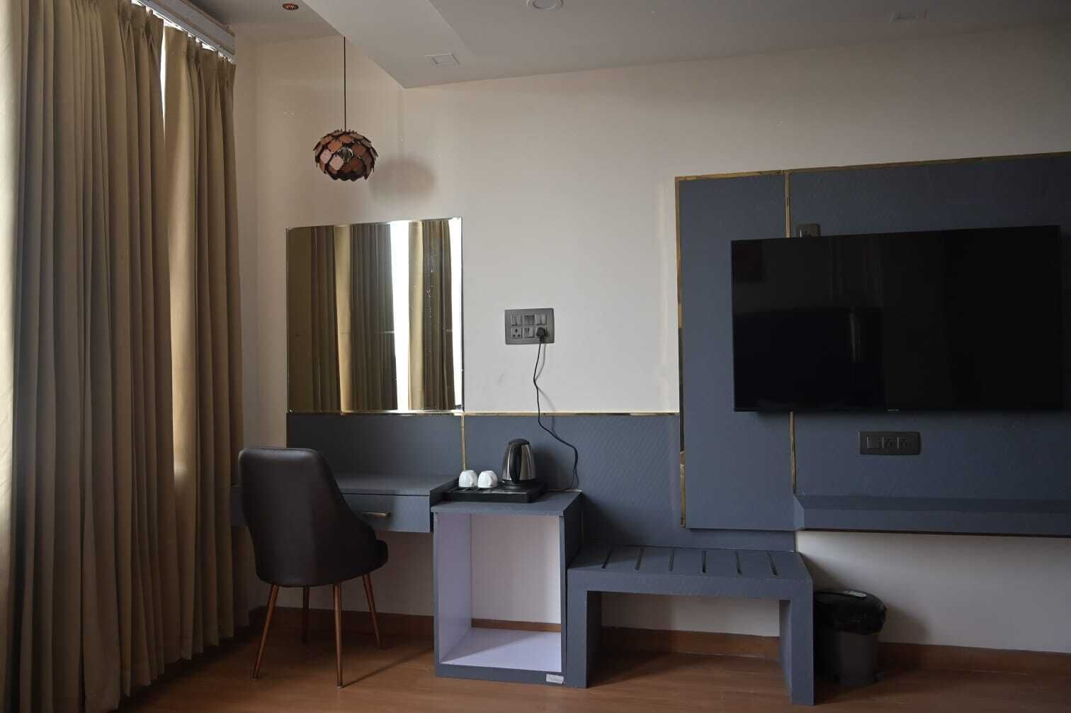 Quarto de hotel com secretária, cadeira, televisão e cortinas.