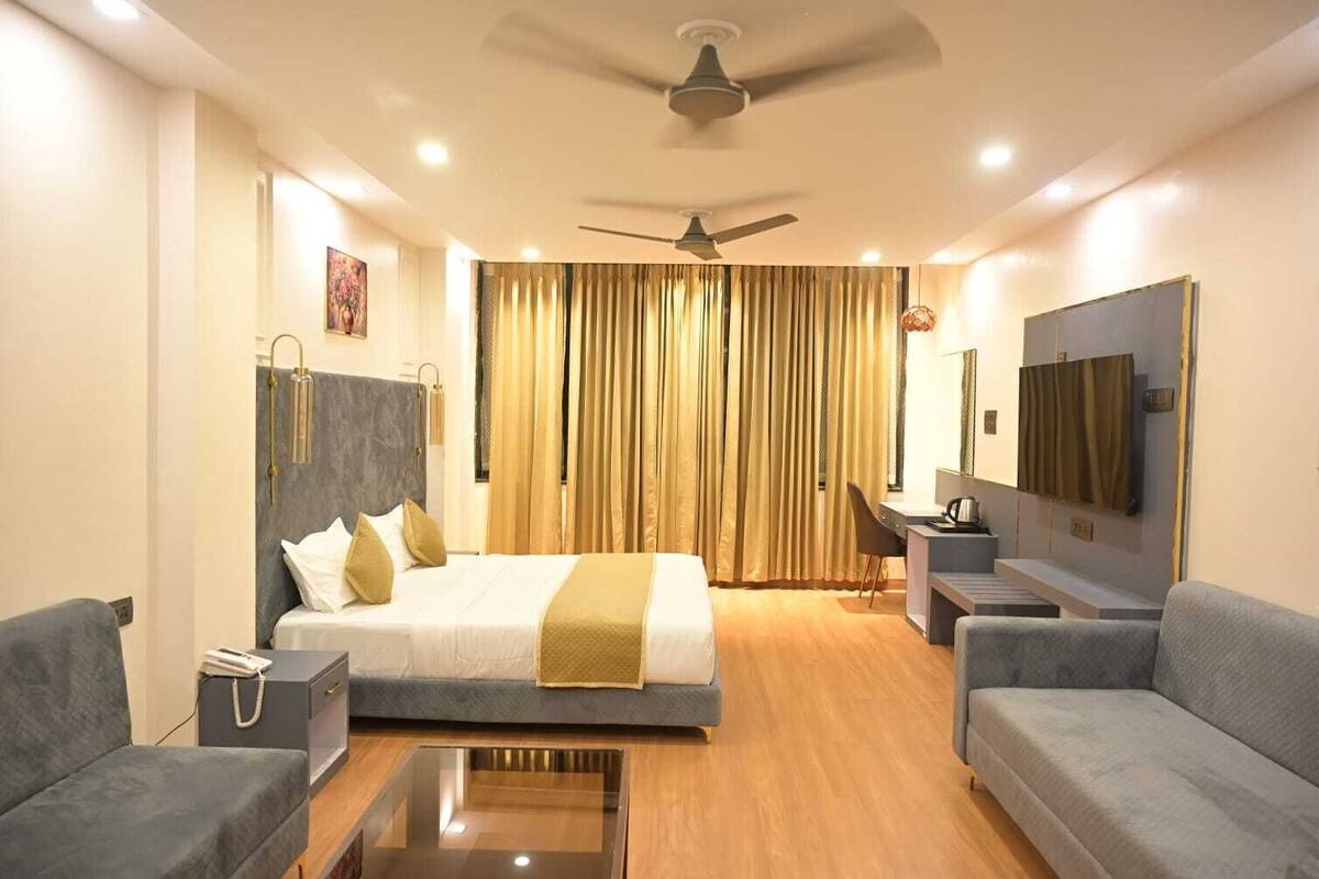 A hotel room with a bed, two sofas, a desk, a TV, and a ceiling fan.