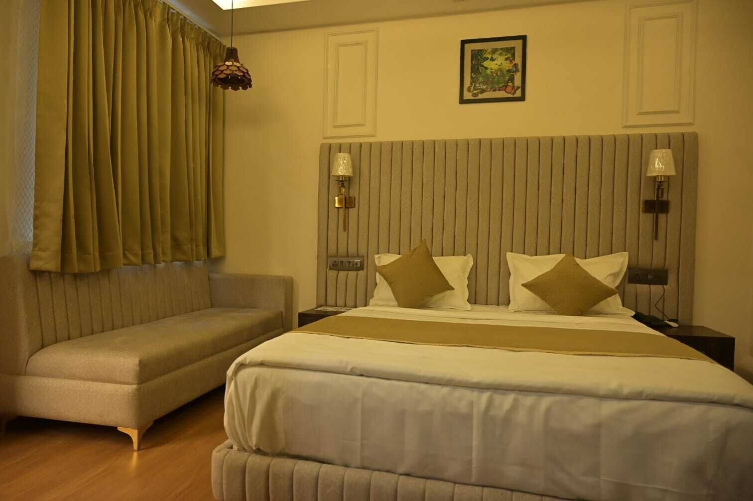 A hotel room with a bed, a sofa, a nightstand, and a wall-mounted lamp.