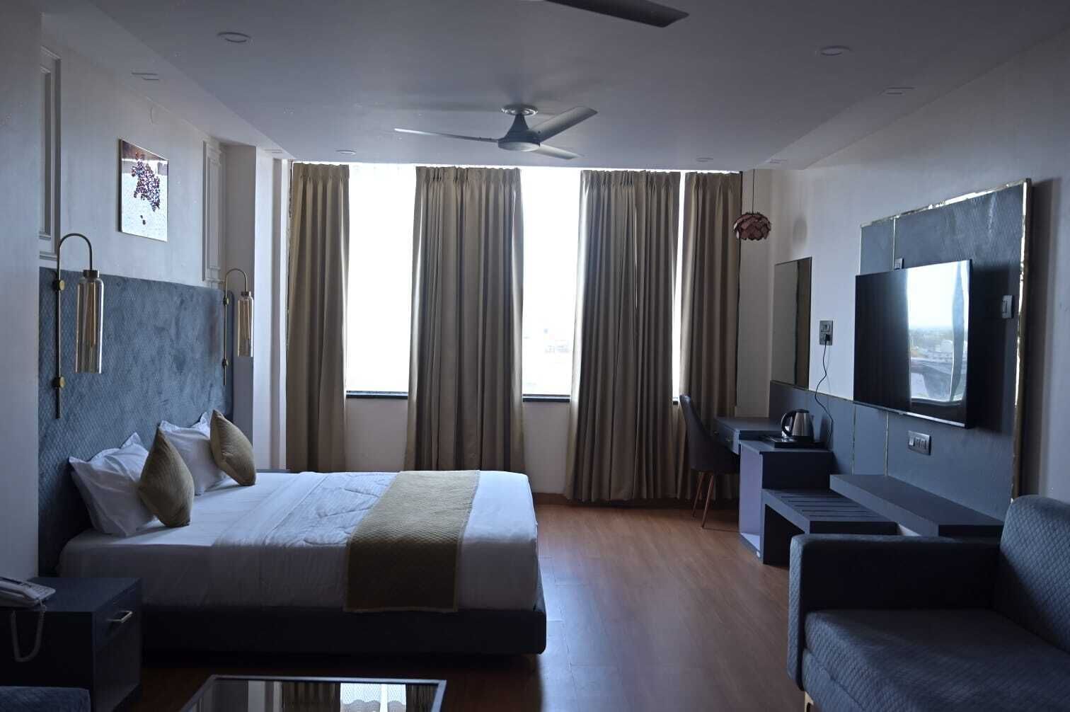 A modern hotel room with a bed, a desk, a chair, a television, and a ceiling fan.