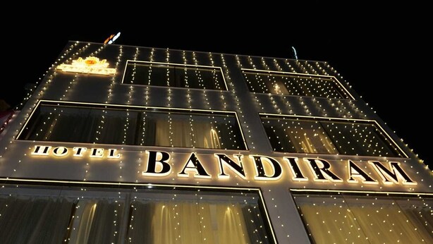 Un hotel de varios pisos con el nombre 'HOTEL BANDIRAM' iluminado en su fachada.