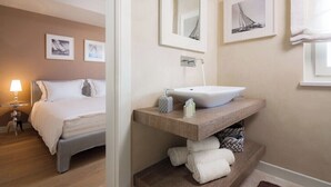 A hotel room with a bed, a bedside table with a lamp, a wooden vanity with a sink, and framed artwork on the walls. - Villa Pia by Nova Villas (Vabriga)
