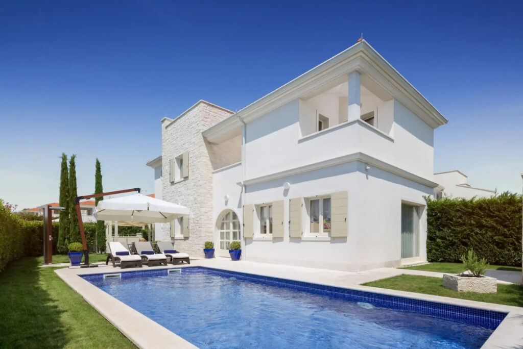 A two-story house with a swimming pool, a covered outdoor seating area, and a well-maintained lawn.