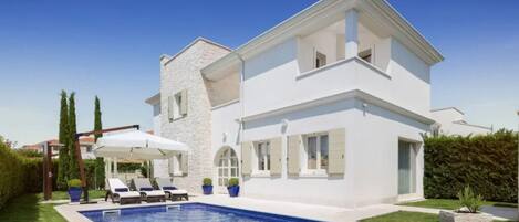 A two-story house with a swimming pool, a covered outdoor seating area, and a well-maintained lawn.