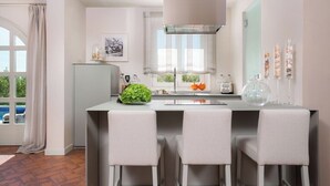 A modern kitchen with a central island, bar stools, a refrigerator, and a window with a view of a swimming pool. - Villa Pia by Nova Villas (Vabriga)