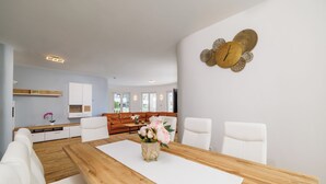 Una sala moderna con una mesa de comedor de madera, sillas blancas, un sofá blanco y un reloj de pared decorativo.
