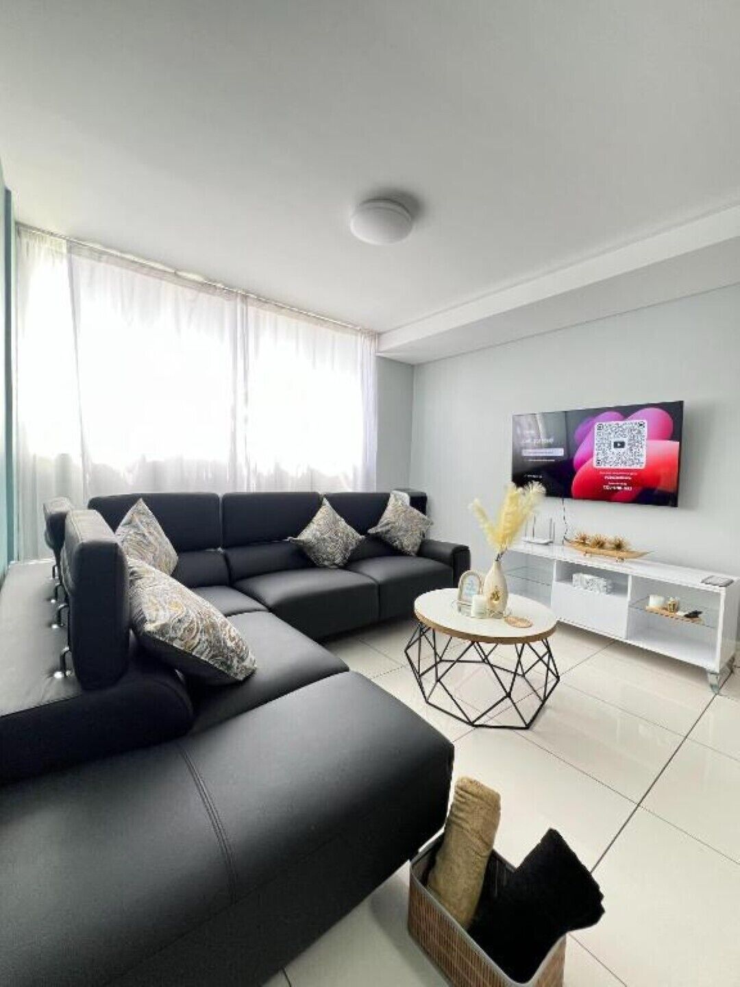 Uma sala de estar moderna com um sofá seccional, uma mesa de centro e uma TV fixada na parede.