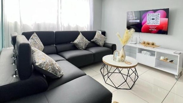 Uma sala de estar moderna com um sofá seccional, uma mesa de centro e uma TV fixada na parede.