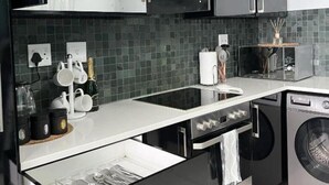 Uma cozinha moderna com armários pretos, bancada branca, máquina de lavar embutida e armário superior com portas de vidro.