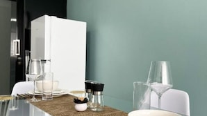 Uma área de jantar moderna com uma mesa de vidro, cadeiras brancas e um frigorífico branco.