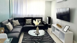 Uma sala de estar moderna com um sofá seccional, uma mesa de centro de vidro, uma TV de tela plana e um móvel de entretenimento branco.
