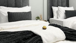 Quarto moderno com duas camas, cabeceiras revestidas de cinza, roupa de cama branca e um cobertor preto.