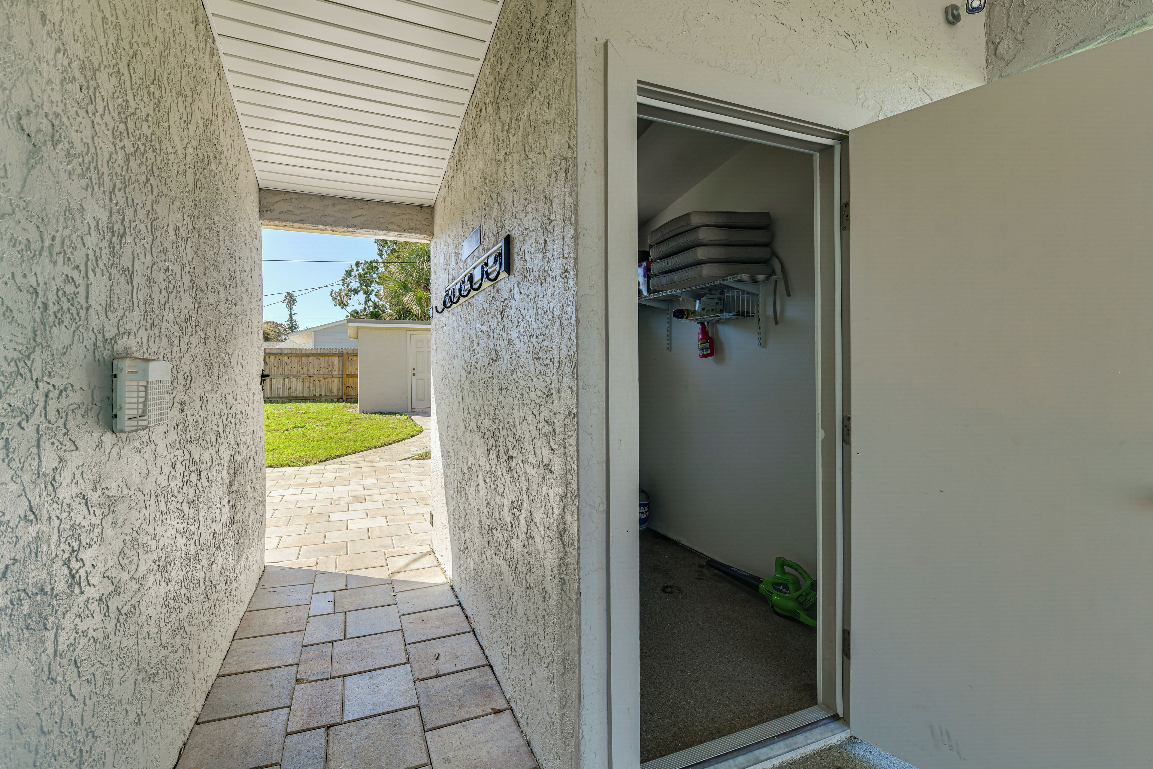 Un couloir étroit avec une porte donnant sur un garage, un extincteur fixé au mur et une petite marche menant à l’extérieur.